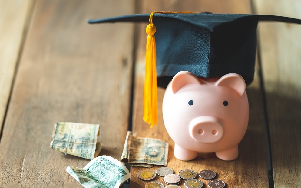 piggy bank with graduation cap on desk with dollar bills and coins