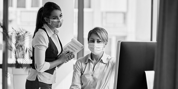 Two female business owners with face masks on looking at a computer screen