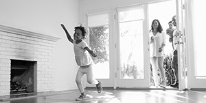 little girl pretending to fly in her new home while her parents and baby brother watch from the doorway