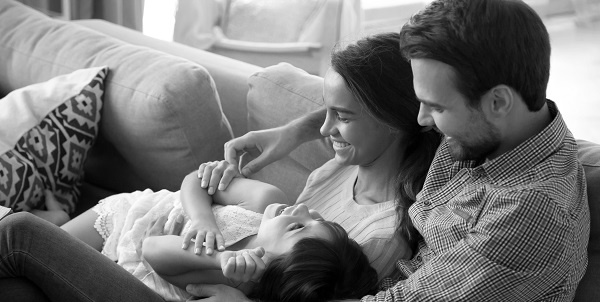 young couple and their daughter laughing and cuddling on their couch at home