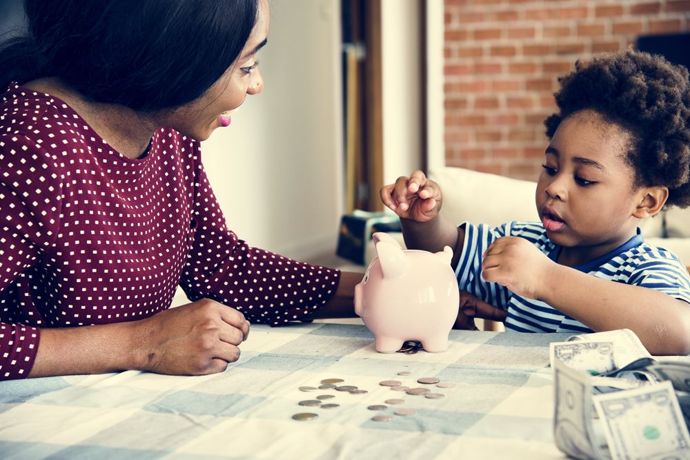 mother showing her toddler son how to count change with coins and a piggy bank