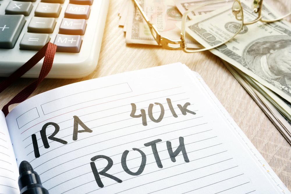 IRA, 401k, and Roth written on a sheet of note paper, surrounded by money and a calculator