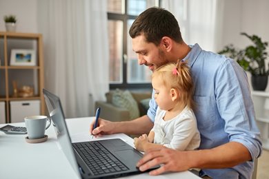 Man working on laptop with toddler in his lap