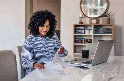 woman at desk looking through paper work with laptop