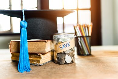 jar with coins labeled "save" on desk with books and graduation cap