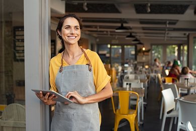 woman standing at entrance of café with tablet 