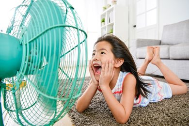 young girl laying on floor of home laughing into the breeze from a cooling fan