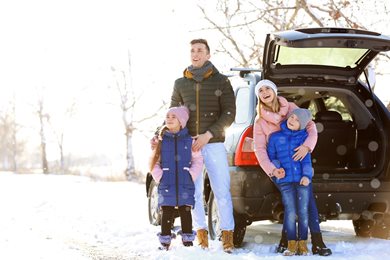 family outside of car in the snow