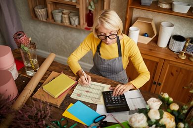 woman sitting as desk surrounded by flowers using a calculator