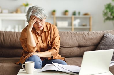 stressed woman at a coffee table with her laptop and a pile of bills