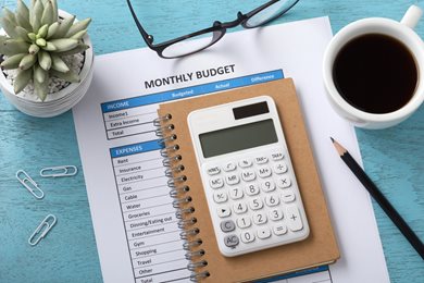 monthly budget, notebook, calculator, pencil, and plant on blue desk