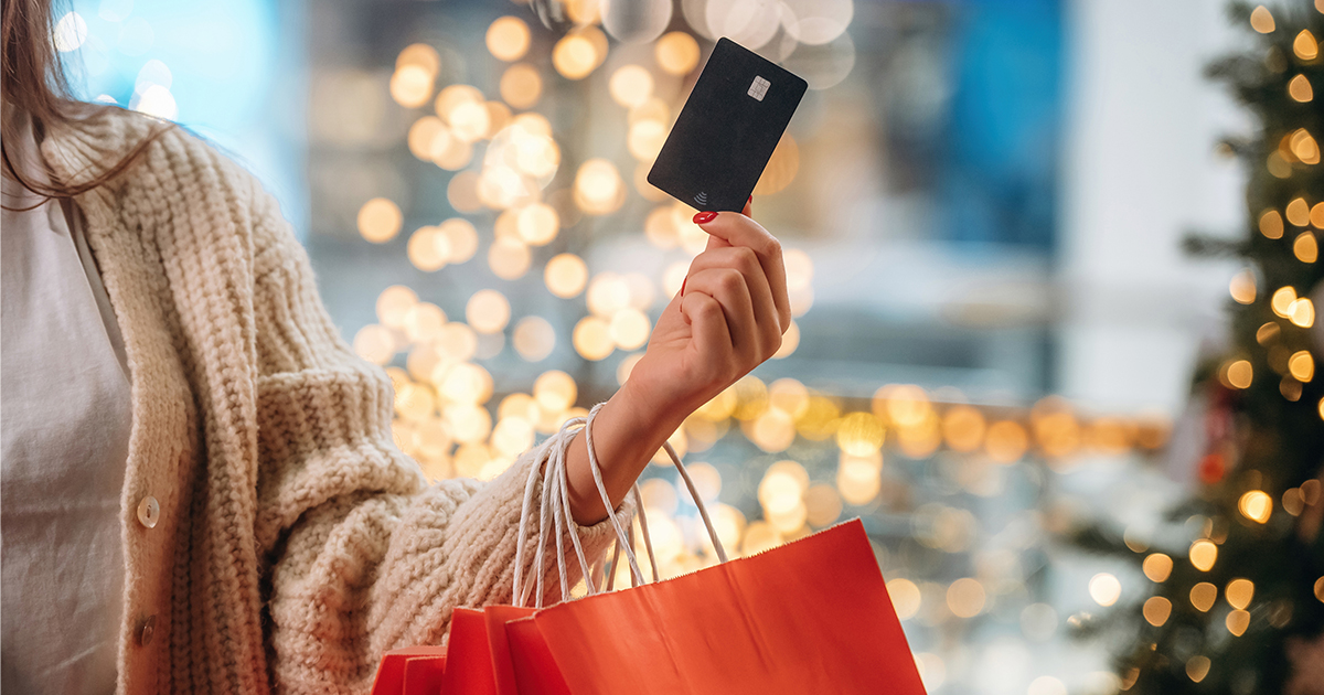 person holding up card payment with shopping bags on arm