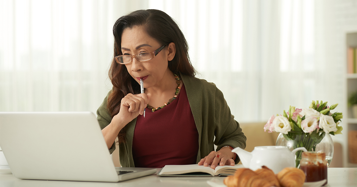 woman sitting at computer with notebook and pen