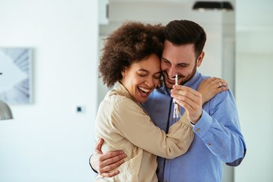 young homebuyers hugging and smiling, holding the key to their first home