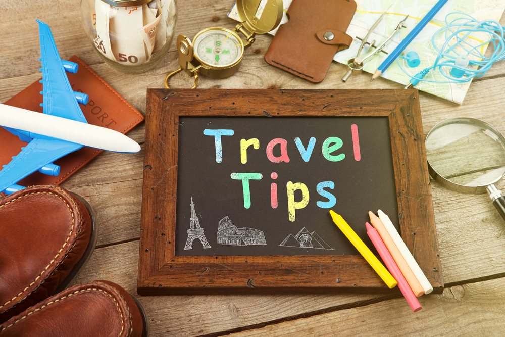 travel tips written on chalk board surrounded by travel accessories and toy plane