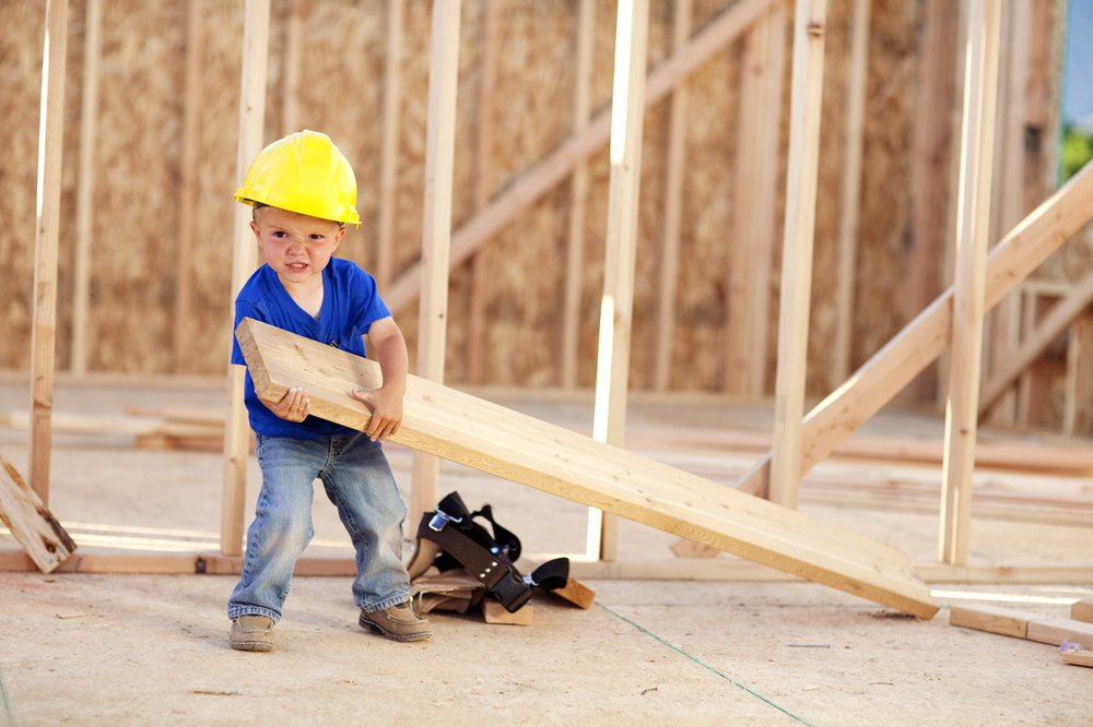 little boy wearing hardhat holding a piece of plywood