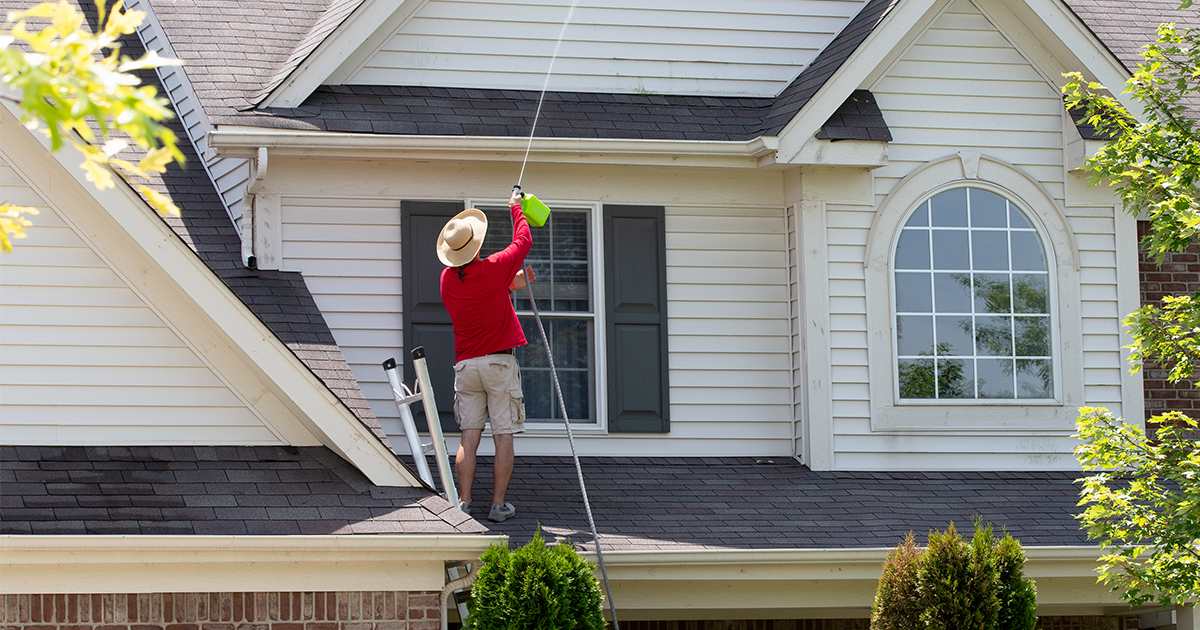 person on roof of home cleaning siding